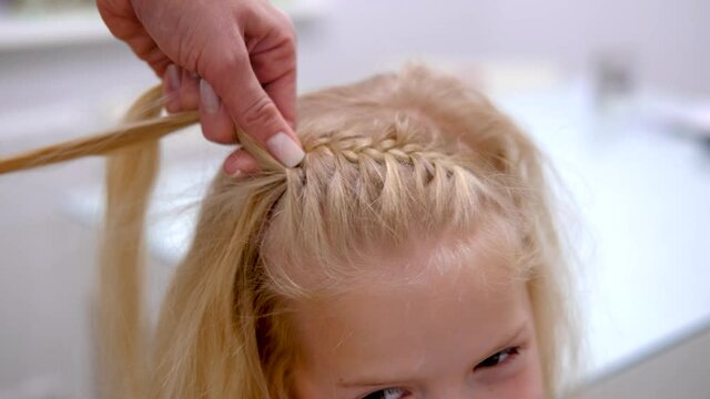 4k. Mother braids daughter pigtails on blonde hair head. Process of braiding weaves braids on head. hands close up.