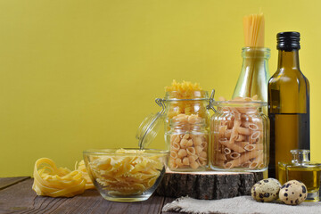Different types of pasta in glass containers on a wooden table on a yellow background