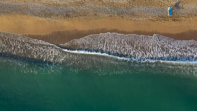 Aerial footage of turquiose sea waves breaking on sandy coastline. Sunny summer day at the beach