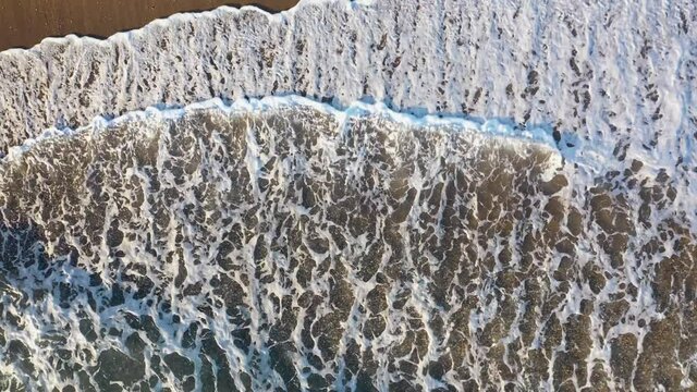 Aerial view of transparent sea waves reaching sandy beach. Sunny summer day 