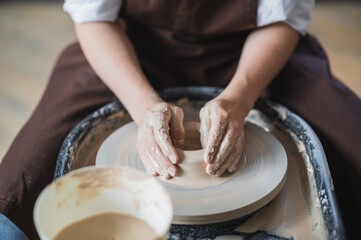 Female potter makes a pot on the pottery wheel close-up.
