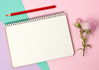 open notebook with white sheets and pink rose on a blue pink background