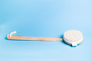 wooden brush for dry body massage on a light blue background, place copy, peeling and body care at home