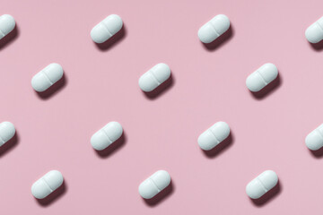 white pills or capsules lie in rows diagonal on pink background top view pattern