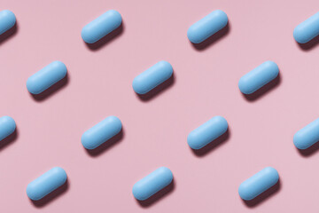 blue pills or capsules lie in rows diagonal on pink background top view pattern