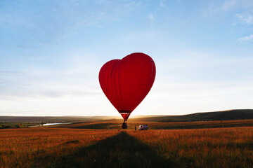 Fototapeta na wymiar hot Red air balloon heart shape flying into sunset over valley landing or taking off
