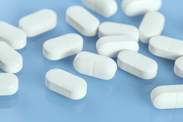 Medical background of many white capsule tablets or pills on blue table. Close up. Healthcare pharmacy and medicine concept with copy space Painkillers or prescription drugs consumption