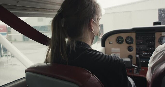 Woman copilot smile with face mask in cockpit of parked small airplane plane aircraft first flight instructions during virus covid 19 coronavirus pandemic outbreak new normal