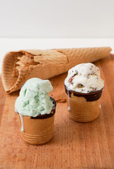 Melting mint craft flavor ice-cream in waffle cups glazed with chocolate and cone on wooden board. High quality vertical photo