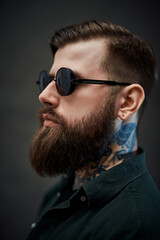 Profile of a young bearded barber with tattoo on his neck in a dark studio