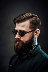 Obraz premium Closeup portrait of a cool bearded male in sunglasses on a dark background
