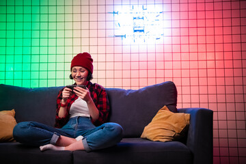 Portrait young teenager hipster girl using smart mobile phone on sofa with pillows in living room...