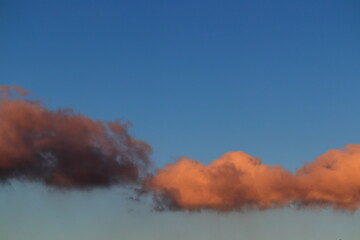 a cloud shaded with brown and another shaded with orange, floating together under a blue sky.