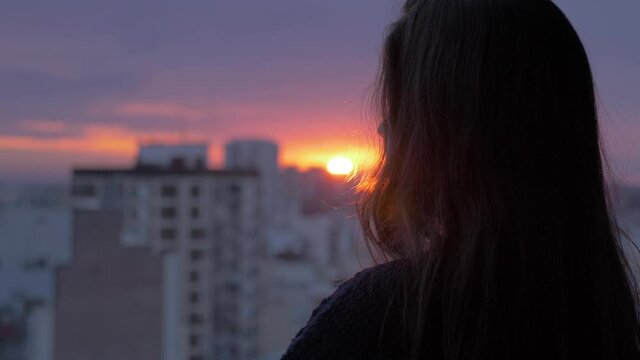 Woman looks out at urban city sunset in the distance as day turns to night Golden Hour View With Clouds 4K Slow Motion
