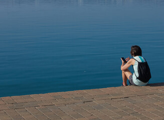 chica joven sentada mirando su movil al lado del mar