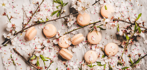 Food texture, wallpaper and background. Flat-lay of sweet macaron cookies and spring blossom flowers over white marble background, top view, wide composition