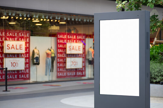 Blank white screen city sale advertisement billboard lightbox mockup. Street poster advertisement light board mock up with blurred female fashion store background.