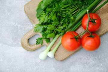 Wooden cutting board with fresh vegetables: tomatoes, parsley, green onion. Healthy organic food, salad ingredients top view