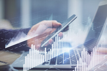 Double exposure of man's hands holding and using a phone and financial graph drawing. Analysis concept.