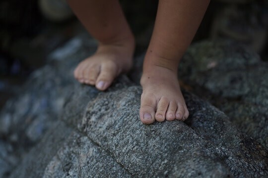 A closeup of a little boys bare feet that is balancing on the edge of a rough rock to convey a dangerous situation.