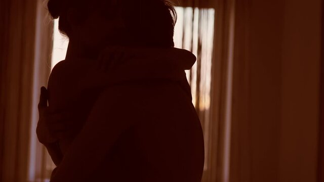 silhouette two toung lovers touching, ambracing and kissing each other soft and tenderly against window with warm sunset sunlight. boy and girl in cozy bedroom before first sex