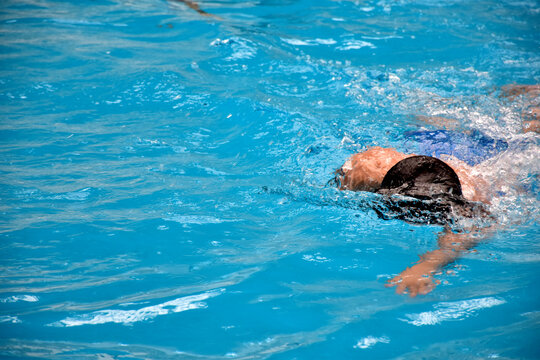 Young boy swimming Freestyle posture in the blue water pool.