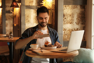 Young blogger taking picture of dessert at table in cafe