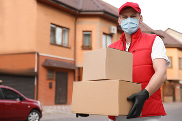 Courier in protective mask and gloves with boxes near house outdoors. Delivery service during coronavirus quarantine