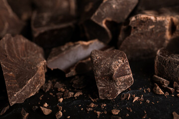 Pieces of dark chocolate on black table, closeup