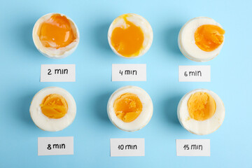 Different cooking time and readiness stages of boiled chicken eggs on light blue background, flat lay