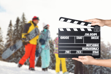 Assistant holding clapperboard and people on snowy slope, closeup. Cinema production