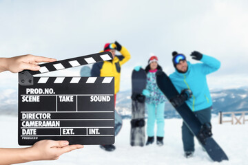Assistant holding clapperboard and people in snowy mountains, closeup. Cinema production