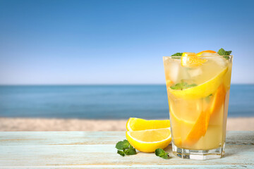 Citrus lemonade with ice cubes on wooden table near sea, space for text
