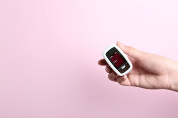 Woman holding fingertip pulse oximeter on pink background, closeup. Space for text