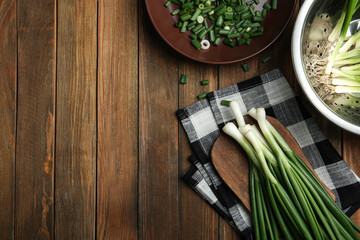 Fresh green spring onions on wooden table, flat lay. Space for text