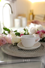 Fototapeta na wymiar Beautiful peonies and cup of tea on kitchen counter