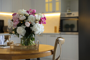 Beautiful peonies in vase on wooden table in kitchen. Space for text