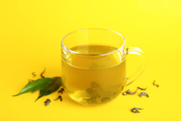 Cup of green tea and leaves on yellow background