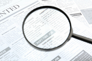 Looking through magnifying glass at newspaper, closeup. Job search concept