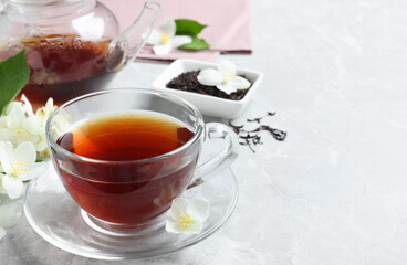 Cup of tea and fresh jasmine flowers on light grey marble table. Space for text