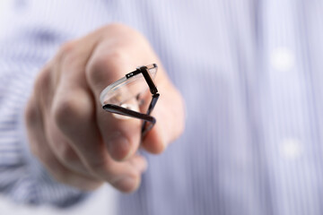 extreme closeup of a man holding a pair of reading glasses pointing at the camera