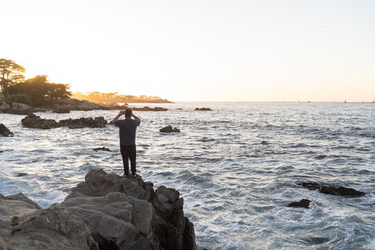 man taking photo of sunset while standing on rocks