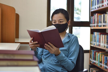 Woman reading a book in library with face mask.