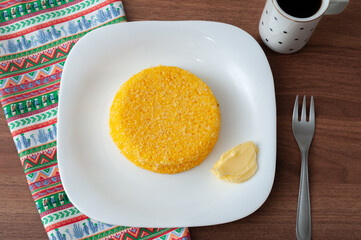 tasteful and colorful brazilian corn couscous served with a cup of coffee on a wooden table