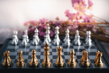 Front view of chess game on chessboard with purple flowers blur background.