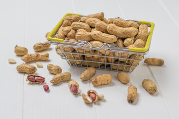A basket of whole and peeled peanuts on a white wooden table.