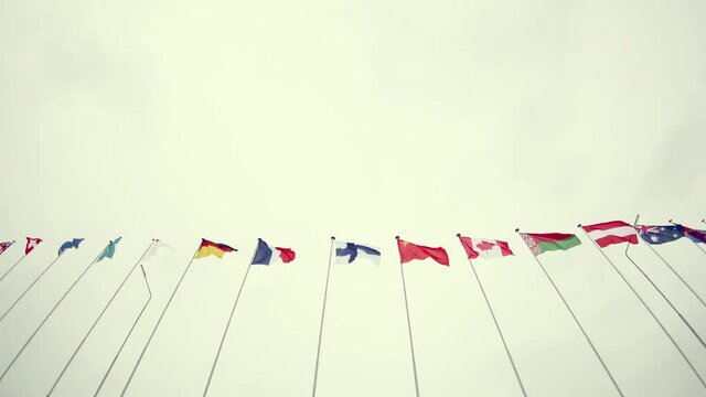 Various world flags flying on flagpoles. Wind sways the canvas. View from below. Background is a gloomy sky. Concept of international sports competition, cooperation.