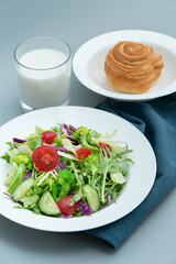A plate of healthy salad and a breakfast bread.A plate of delicious and healthy vegetable salad on a gray concrete floor.