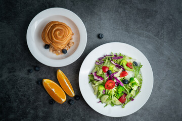 A plate of healthy salad and a breakfast bread.A plate of delicious and healthy vegetable salad on a gray concrete floor.