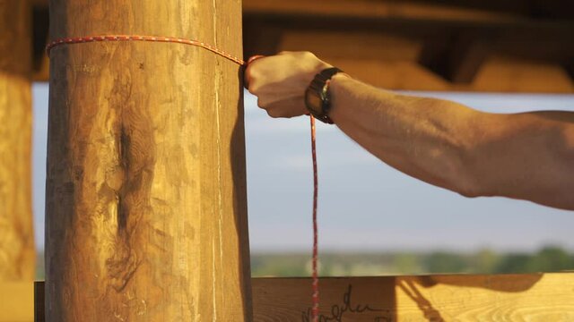 Male hands tying rope to wooden pole of viewing tower during setting up hammock, close up shallow focus shot, Wigry National Park, Suwalszczyzna, Poland
